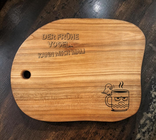 Schwarzwald Gravur natural cherry wood cutting board with engraved text and a grumpy bird with a coffee mug.
